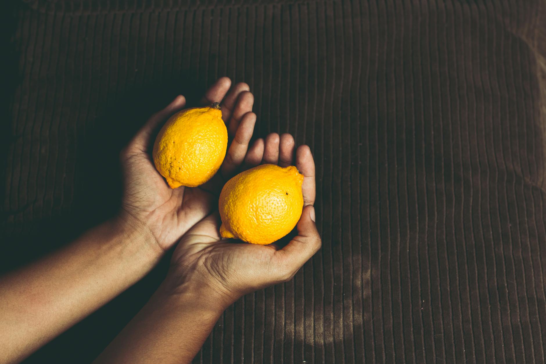 A hand holding a fresh lemon on a soft pink background, symbolizing tenderness and self-care