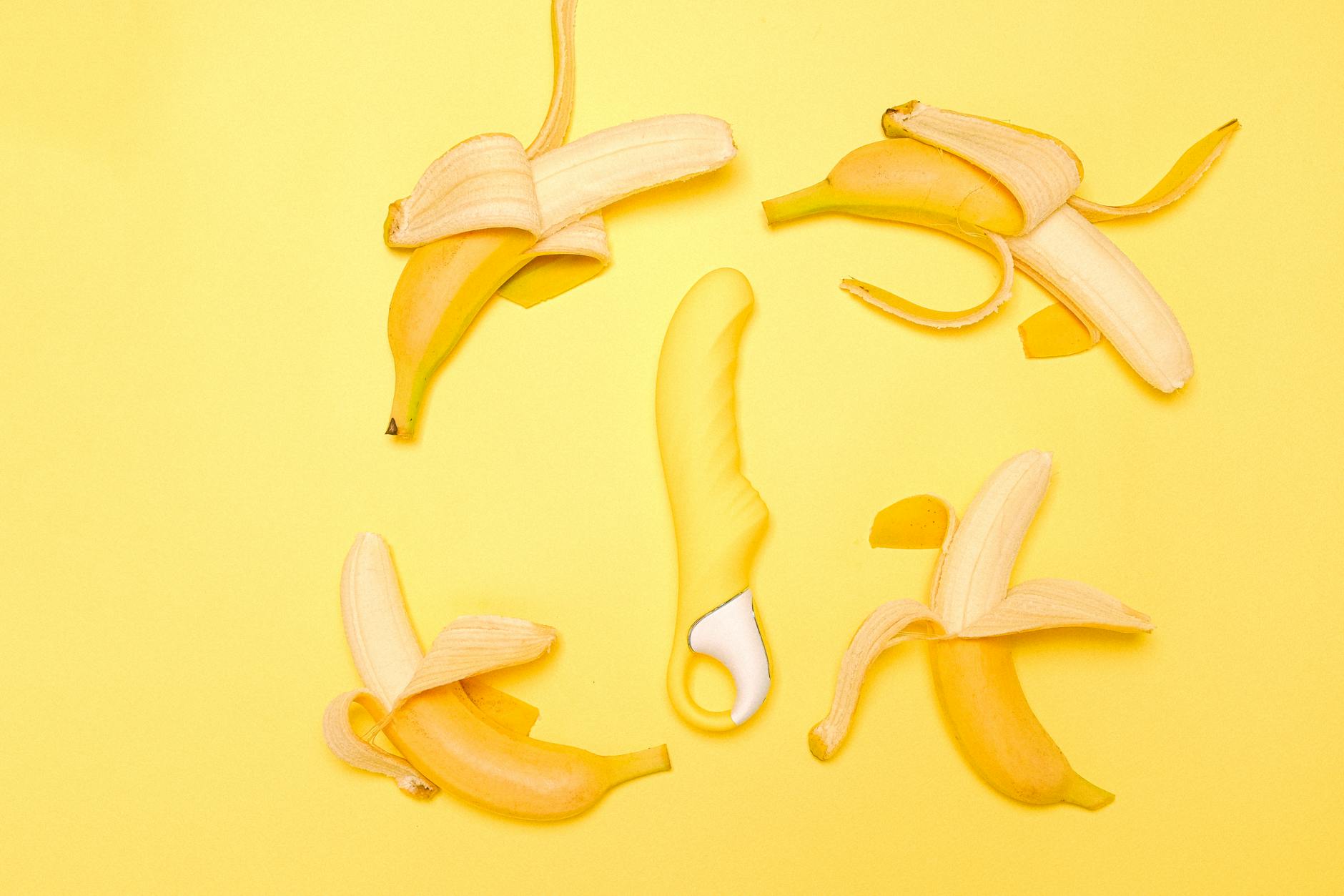 A yellow silicone lemon vibrator surrounded by fresh lemons and bananas on a bright yellow background, symbolizing pleasure and health.