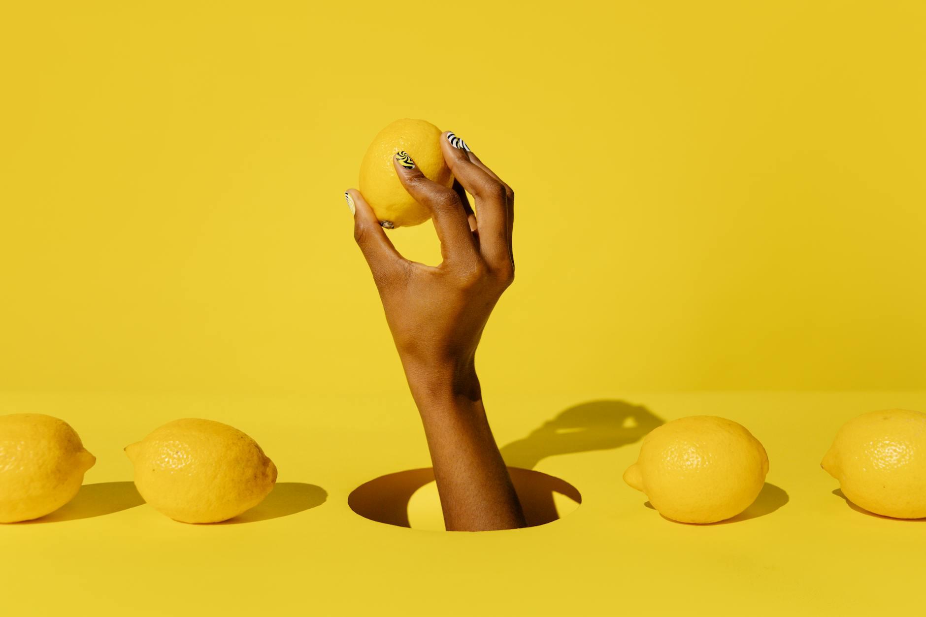 A hand holding a bright lemon against a vivid yellow background, symbolizing fresh begins and pleasure exploration