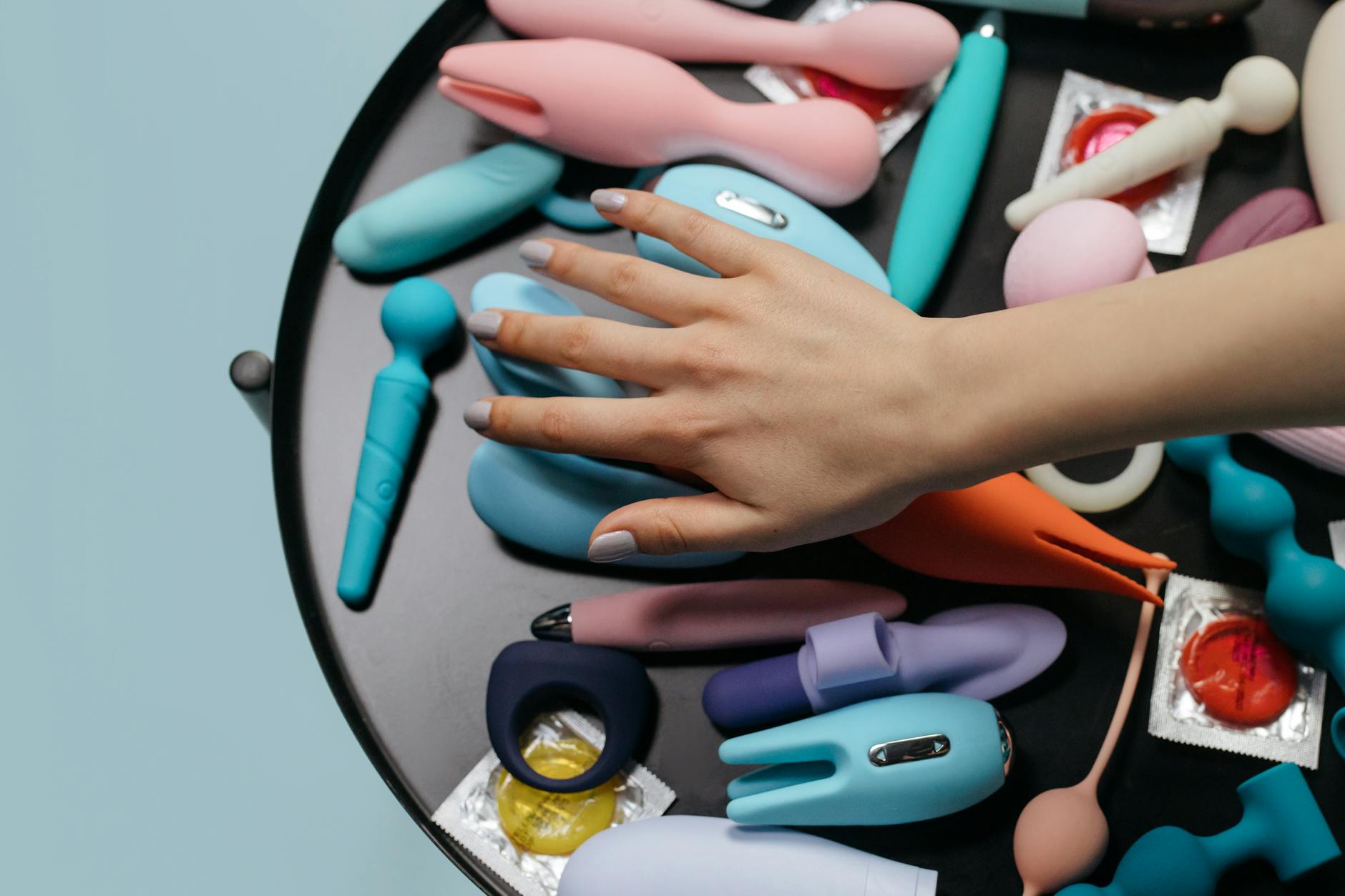 A hand reaching over a variety of colorful Lemon sex toys arranged on a table.