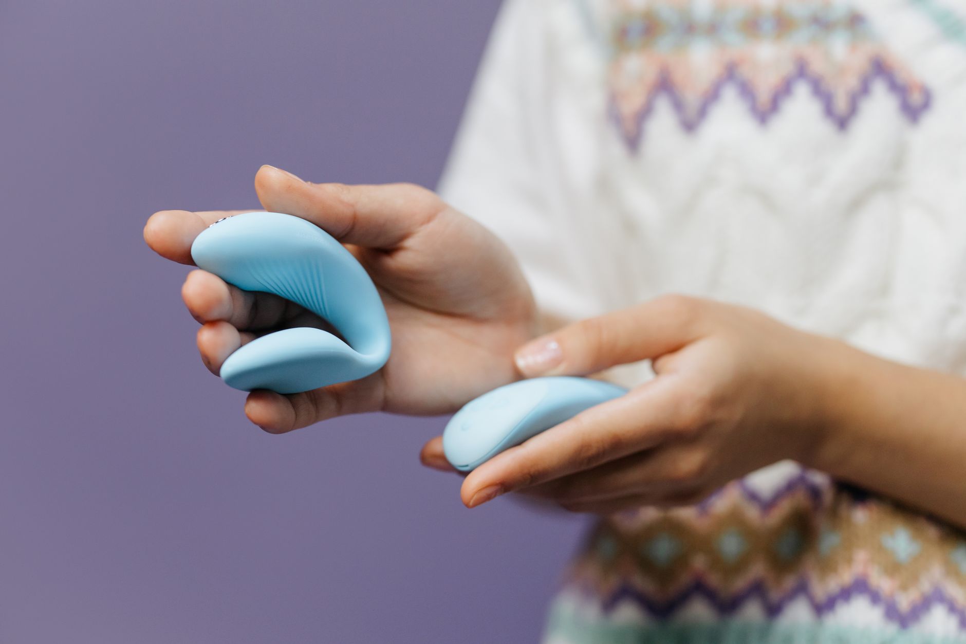 Close-up of hands holding a sleek blue vibrator against a minimalist background.
