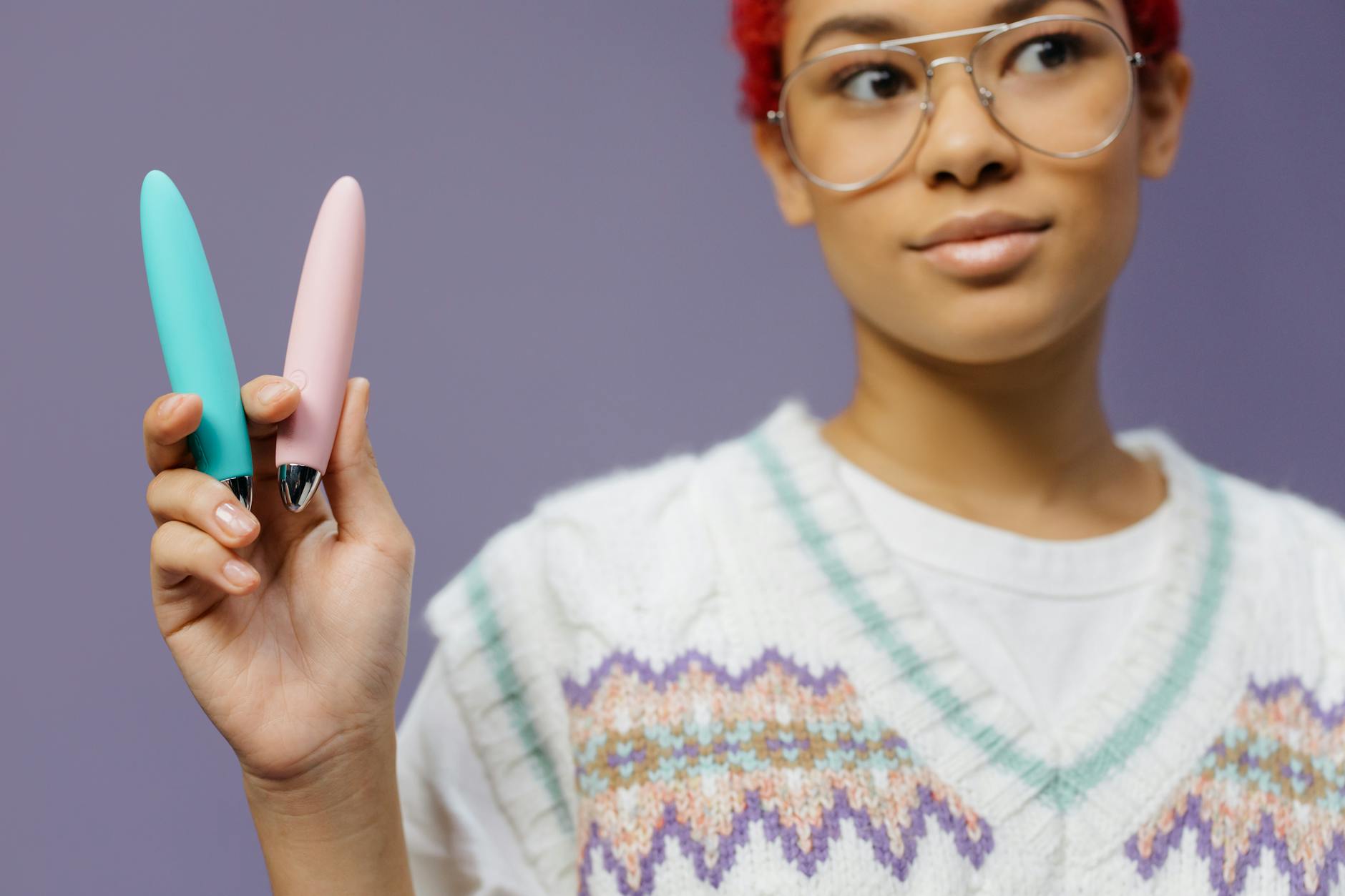 A person holding colorful vibrators against a purple background