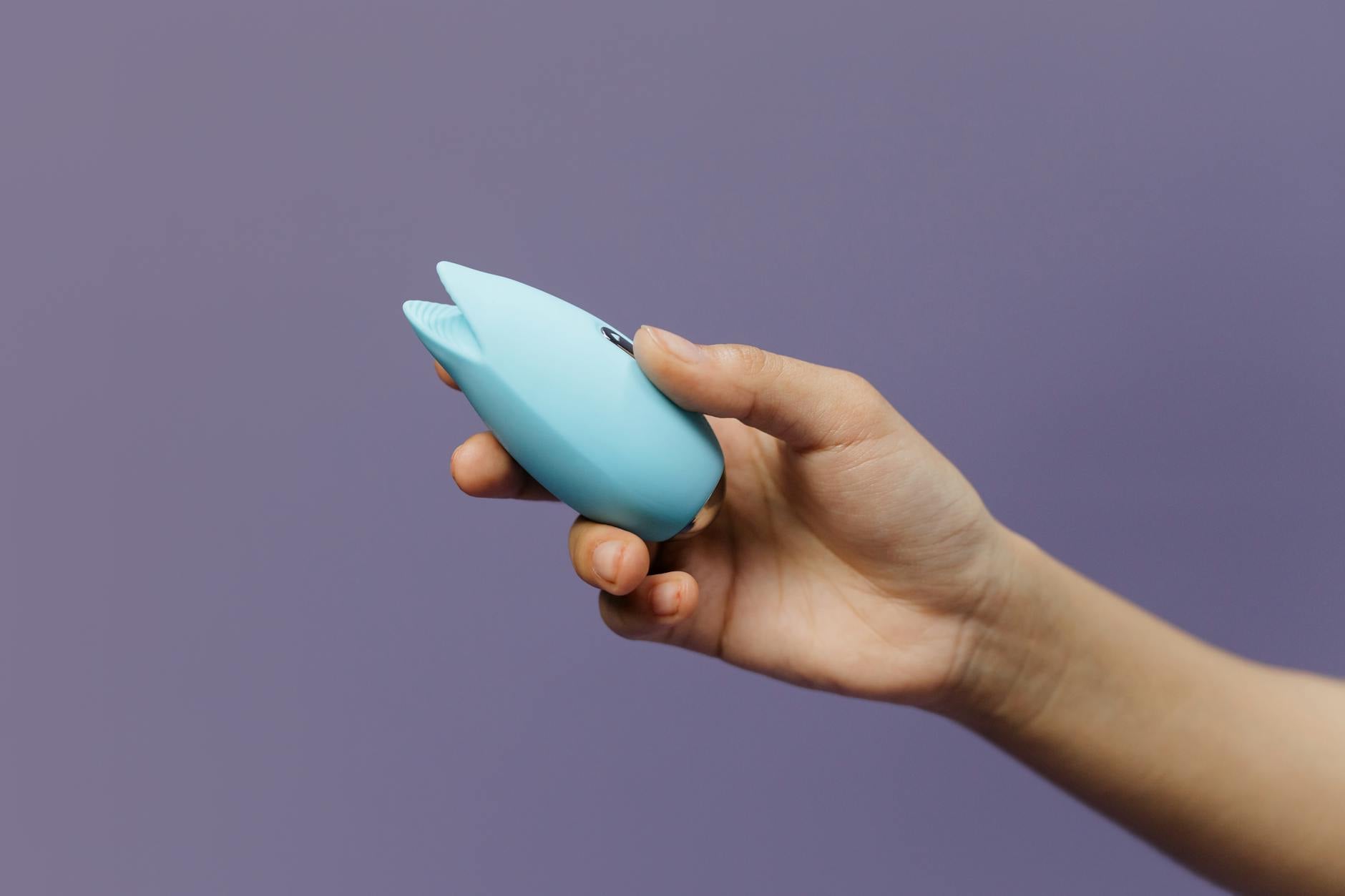 A silicone vibrator held in hand against a solid purple background, promoting pleasure and self-care