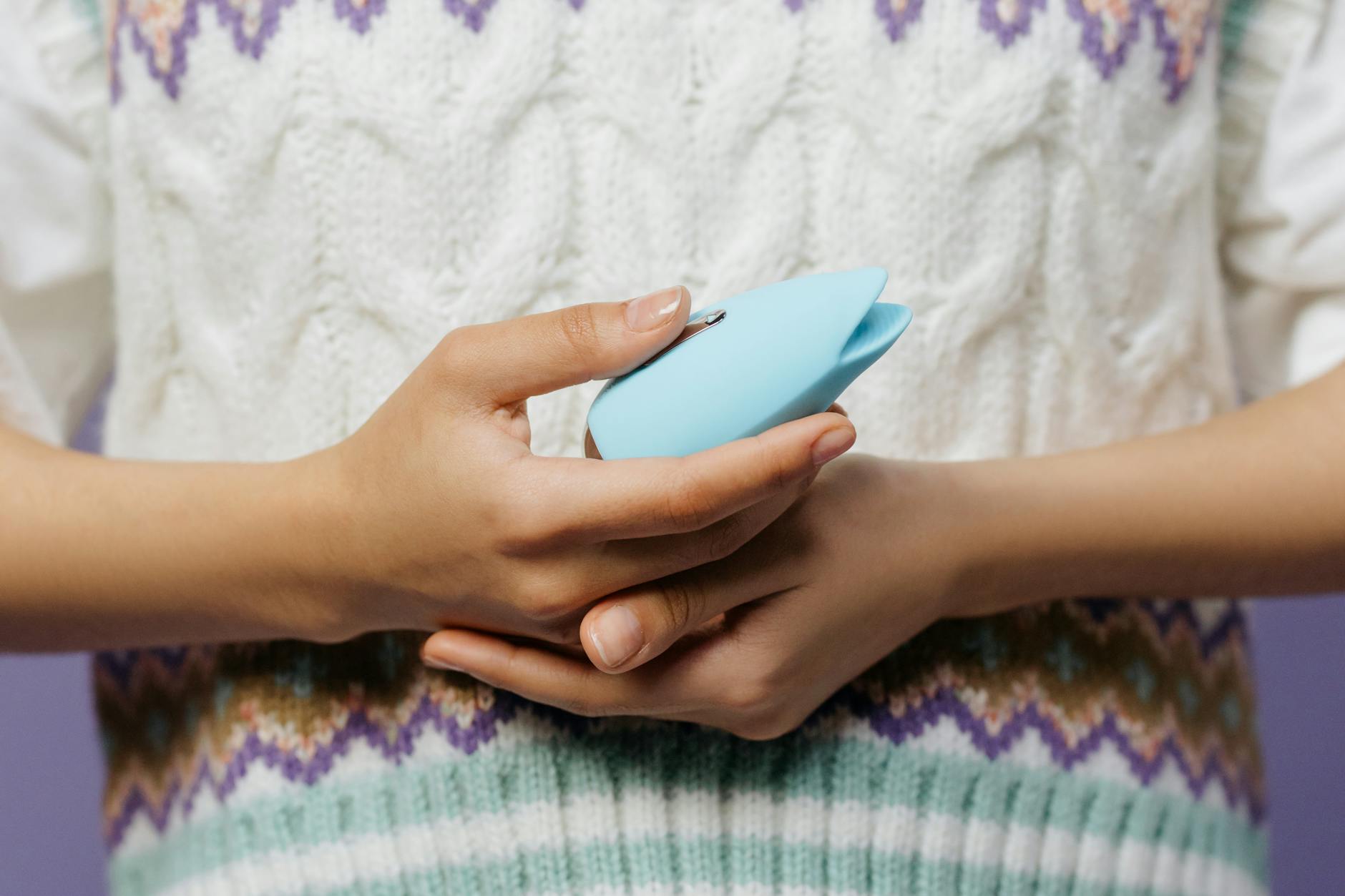 A person holding a blue silicone vibrator against a solid purple background, highlighting modern approaches to self-love and pleasure.